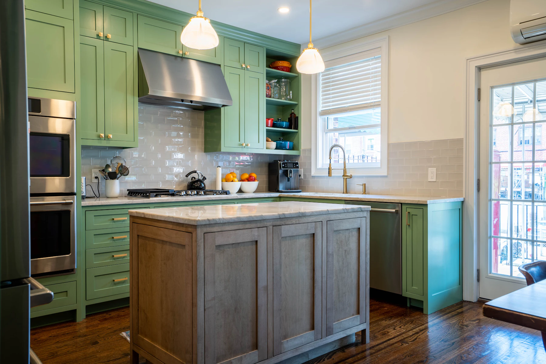 A kitchen with sage green painted cabinets, brass pulls and a natural wood island